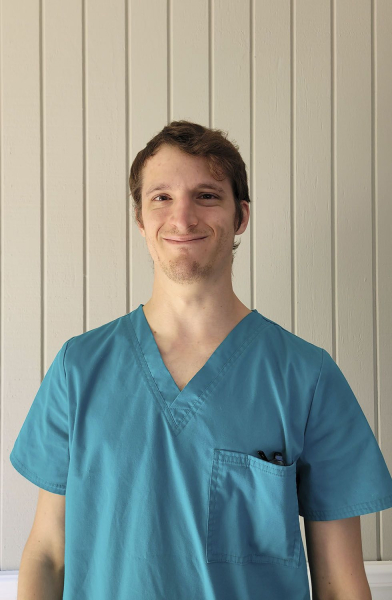 Young male nurse in teal scrubs smiling at the camera.