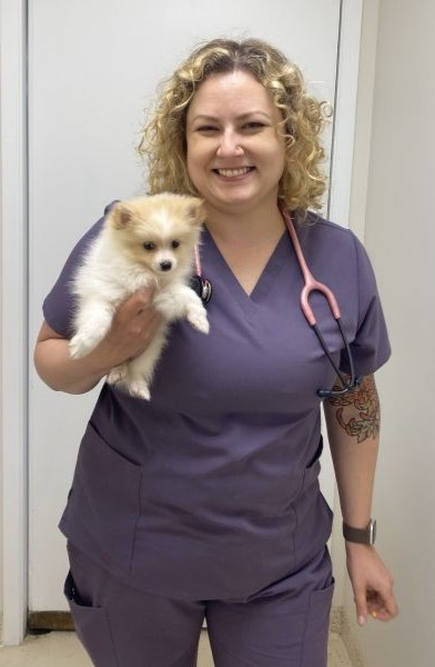 A smiling nurse in scrubs holding a small Pomeranian dog.