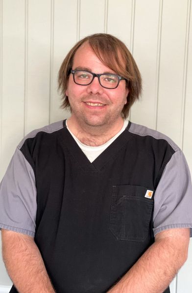 Man with glasses smiling, wearing a dark v-neck shirt with a lighter shirt underneath.