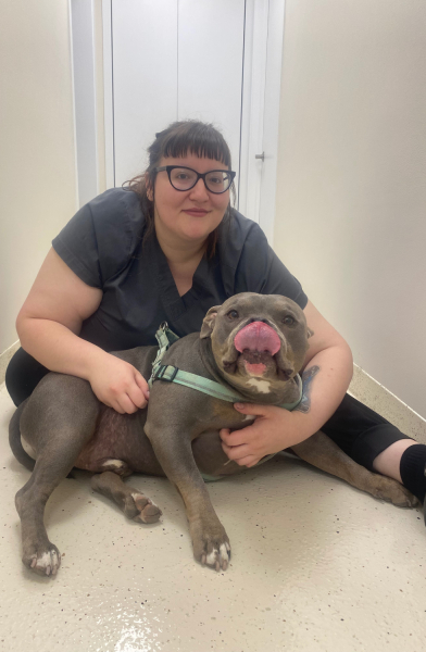Woman in black sitting with a happy grey dog in a hallway.