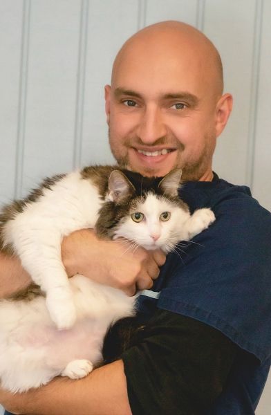 Bald man smiling, holding a large fluffy cat with white and brown fur.