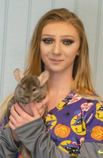 Young woman holding a gray chinchilla in her arms.